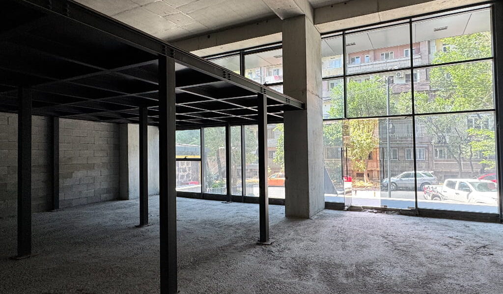 Empty unfinished commercial space with concrete floor and dark steel columns, large glass storefront windows showing cars and trees outside?