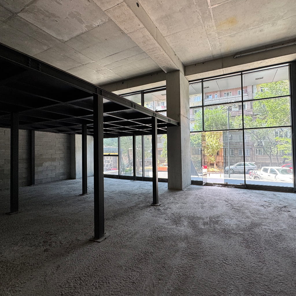 Empty unfinished commercial space with concrete floor and dark steel columns, large glass storefront windows showing cars and trees outside?