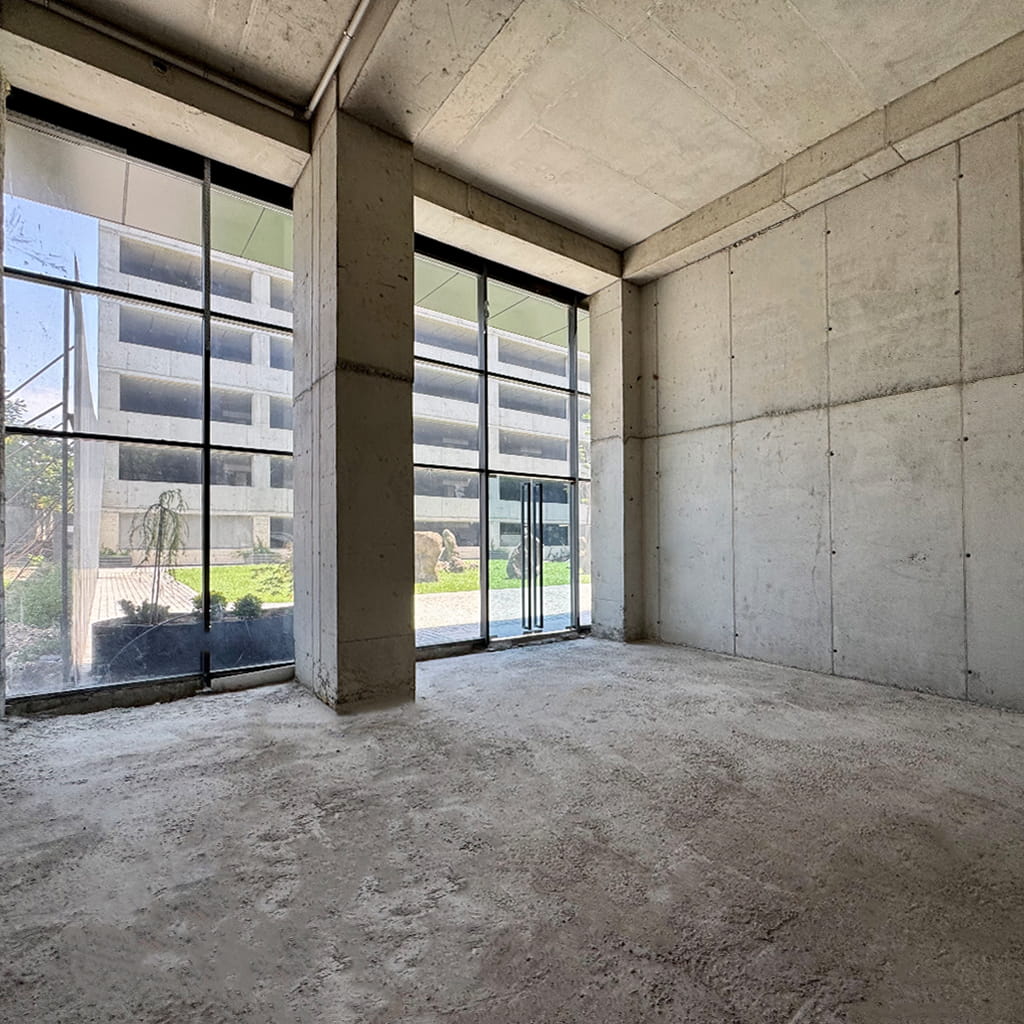 Empty unfinished concrete room with large glass storefront windows and a doorway, daylight outside.