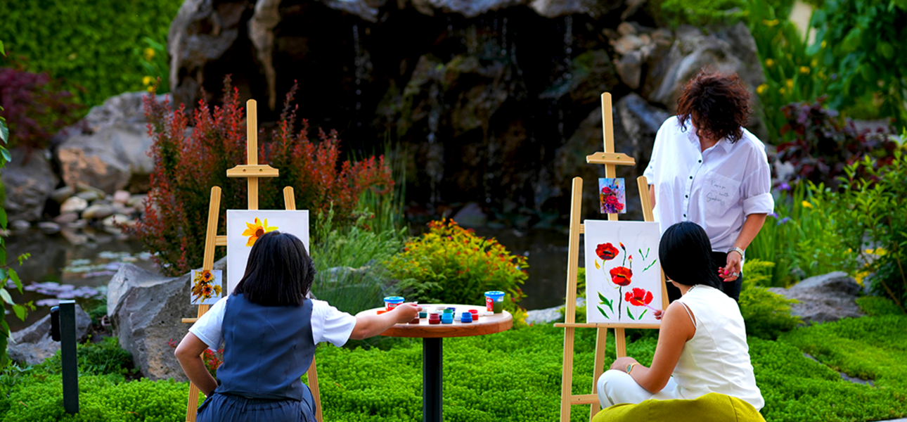 Outdoor painting class with easels and artists painting flowers in a lush garden.
