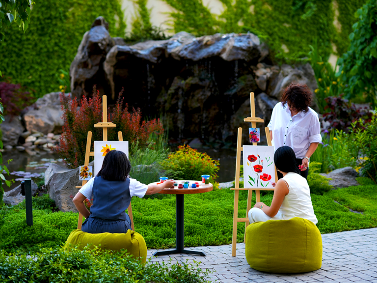 Outdoor painting class with easels and artists painting flowers in a lush garden.