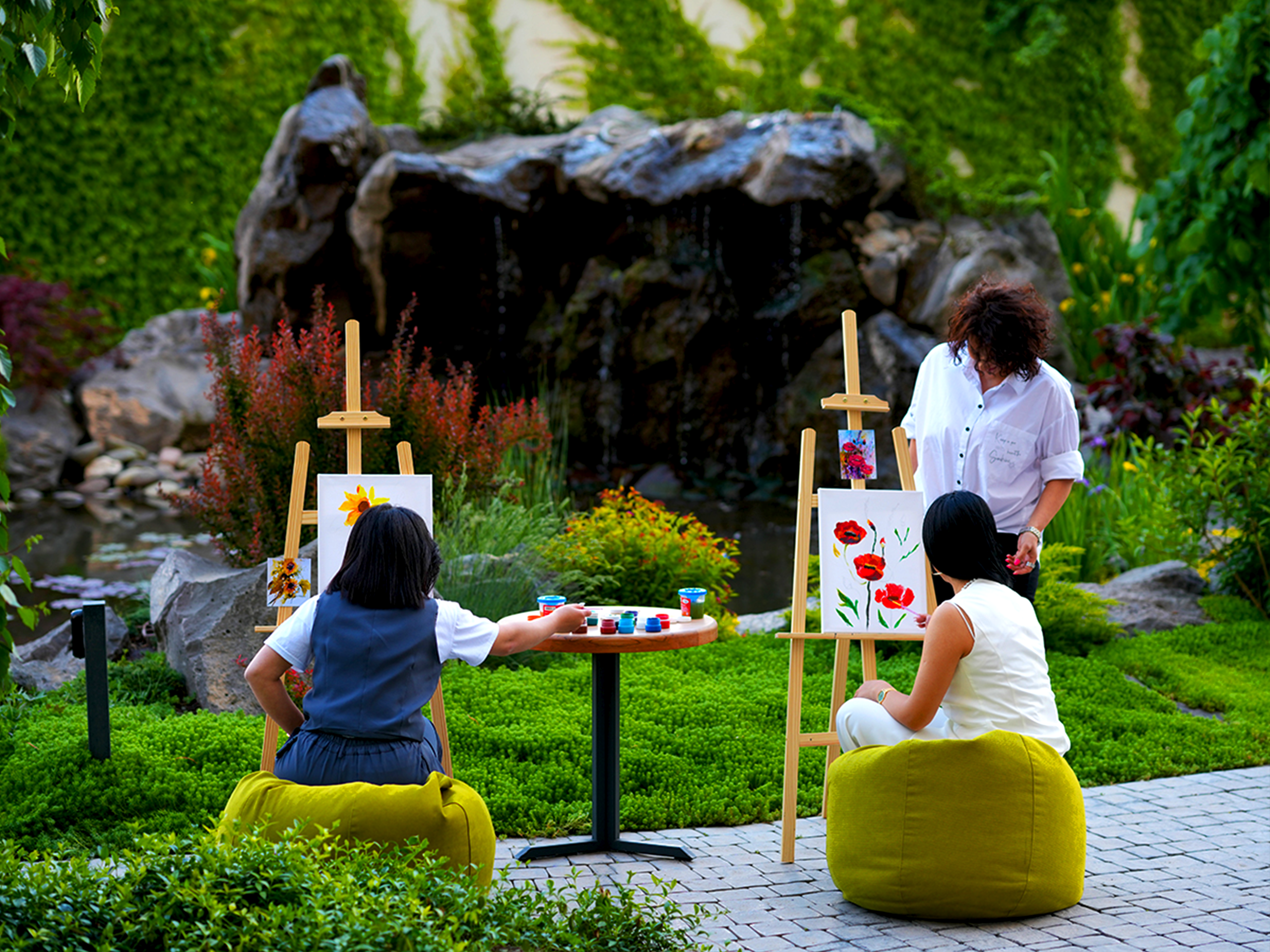 Outdoor painting class with easels and artists painting flowers in a lush garden.